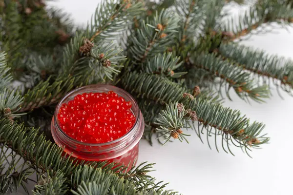 Kırmızı havyar cam bir kavanozda zarif bir şekilde sergileniyor. Taze yeşil dalların üzerinde dinleniyor. Tatil kutlamalarında biraz lüksü sergiliyor..