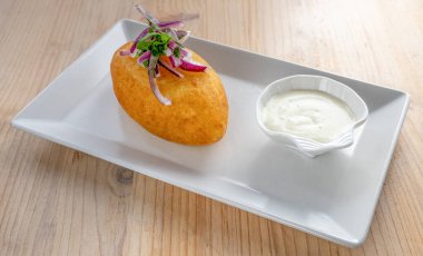  Papa Rellena 'ya yakın plan, patates püresiyle doldurulmuş geleneksel Peru yemeği, kızarmış altın-kahverengi, beyaz bir tabakta mayonez sosu ile servis edilmiş, ahşap bir arka planda izole edilmiş..