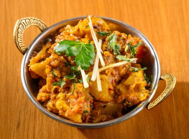 Aloo Gobi Masala geleneksel Hint mutfağı taze karnabahar, patates, soğan sosunda pişirilmiş ve baharatlı taze domates hafif ahşap arka planda izole edilmiş. 