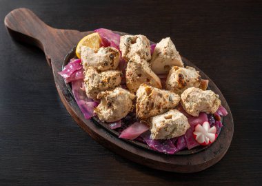 Malai Tikka 'nın yakın çekimi, yoğurt, krema, kaju, kakule, beyaz biber ve baharatla marine edilmiş geleneksel Hint tavuk parçaları, soğanla servis edilen cızırdayan bir tabakta, koyu bir ahşap arka planda izole edilmiş..