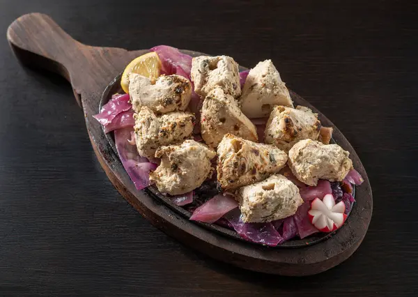 Malai Tikka 'nın yakın çekimi, yoğurt, krema, kaju, kakule, beyaz biber ve baharatla marine edilmiş geleneksel Hint tavuk parçaları, soğanla servis edilen cızırdayan bir tabakta, koyu bir ahşap arka planda izole edilmiş..