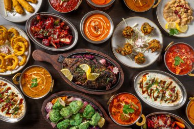 Hint yemeklerinin tipik kompozisyonu köri, naan ve pirinç gibi, koyu ahşap bir masa üzerinde sergilenen sıcak otlatma ışığı, canlı baharatlar ve rustik kaselerde süslemeler.