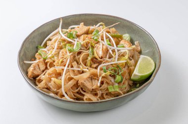 Pirinç eriştesi, sebze, tavuk ve tamarind soslu Pad Thai tabağı, beyaz arka planda yeşil bir seramik kasede servis ediliyor. Parlak, davetkar fotoğraf, Tayland ve Asya mutfağı teması için ideal..