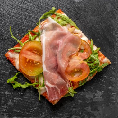 Domatesli İtalyan pizzası, çiğ jambon, mozzarella ve roket. Geleneksel tarz, parlak renkler, basit kompozisyon, iştah açıcı yemek, İtalyan mutfağı teması için mükemmel..