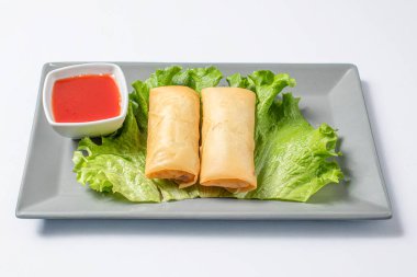 Geleneksel doldurulmuş Çin börekleri taze marulla servis ediliyor, gri bir tabakta beyaz arka planda baharatlı sosla servis ediliyor. Temiz ve asgari estetik bir Asya mutfağı sunan canlı bir yemek..