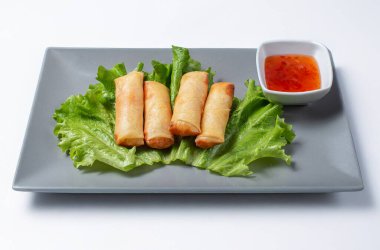 Geleneksel Çin börekleri taze marul yatağında, gri bir tabakta beyaz arka planda baharatlı sos ile servis ediliyor. Canlı, iştah açıcı, otantik Asya tatları sergiliyor.