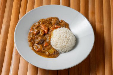 Japon körili pirinci, yumuşak et, havuç ve patates, bambu zemin üzerinde servis edilir. Sıcak, kırsal bir estetik ile geleneksel tatlar sunan doyurucu bir Asya yemeği.