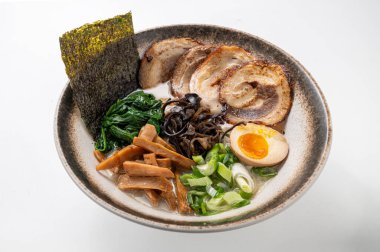 Makarna, domuz göbeği, deniz yosunu, ıspanak, mantar, yumurta ve yeşil soğanlı tonkotsu ramen beyaz arka planda. Çin ve Japon mutfağının sergilendiği zengin, geleneksel bir Asya yemeği.