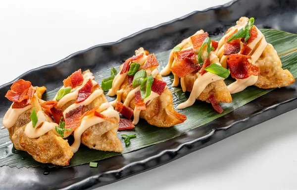 Beyaz arka planda servis edilen mayonez ve pastırmalı gevrek gyoza seramik tepsisinin yakından görüntüsü. Çin mutfağını modern bir kıvrımla harmanlayan lezzetli bir Asya yemeği. Temiz ve asgari estetik içeriyor.