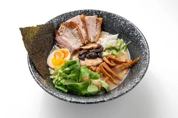 Beyaz zemin üzerinde domuz eti, şehriye, deniz yosunu, mantar, yumurta ve yeşil soğanlı erişte kabı. Canlı, geleneksel bir Asya yemeği. Çin ve Japon mutfağı sergileniyor.