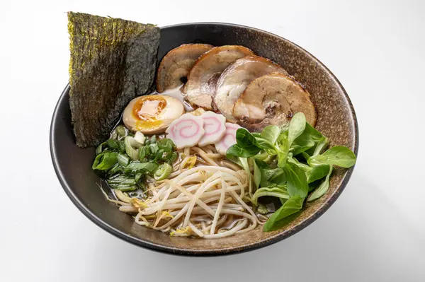 Beyaz arka planda erişteli Shoyu eriştesi, domuz göbeği, yosun, yeşillik, narutomaki, yumurta ve fasulye filizleri. Canlı, geleneksel bir Asya yemeği. Çin ve Japon mutfağı sergileniyor..