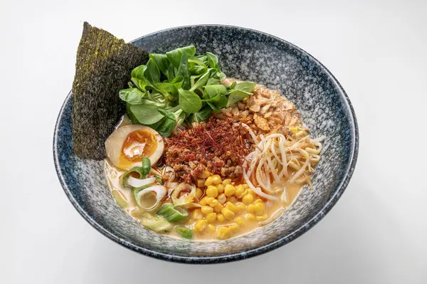 Şehriyeli, yosunlu, yeşillikli, mısırlı, yumurtalı ve kırmızı biberli vejetaryen miso ramen beyaz arka planda. Canlı, geleneksel bir Asya yemeği Çin ve Japon mutfak stillerini sergiliyor.