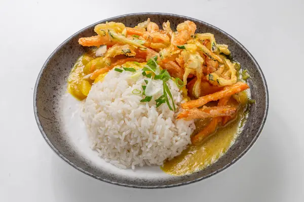 Tempura sebzeli vejetaryen körili pilav, kremalı sos ve yeşil soğanla süslenmiş, beyaz arka planda siyah bir kasede. Canlı, lezzetli bir Asya yemeği..