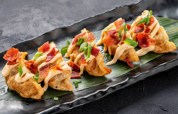 Koyu bir arka planda servis edilen mayonez ve pastırmalı gevrek gyoza seramik tepsisinin yakın plan görüntüsü. Çin mutfağını modern bir kıvrımla harmanlayan lezzetli bir Asya yemeği. Temiz ve asgari estetik içeriyor.