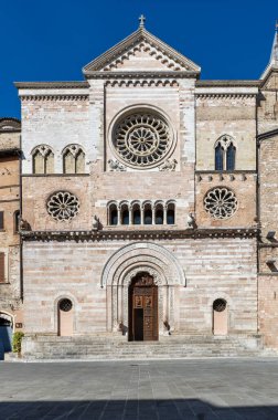 İtalya, Umbria 'daki Foligno Katedrali' nin ortaçağ oymalı yan kapısı. Pembe mermer bantlı Romanesk Gotik kemer, karmaşık oymalar ve güneşli ahşap kapı Foligno, İtalya, 12 Temmuz 2025