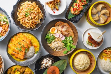 Gyoza, gua bao, ramen, pilav, erişte ve ravioli içeren canlı bir Asya mutfağı kompozisyonu, yukarıdan beyaz arka planda yakalanır. Doğal ışık, bu bereketli sokak yemeği ziyafetinin altını çiziyor.