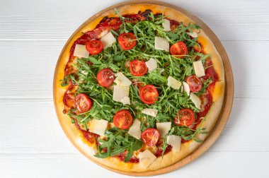 Domates soslu İtalyan pizzası, mozzarella, taze vişneli domates, roka ve parmesan talaşı, yukarıdan beyaz ahşap zemin üzerine atılmış. Yatay, doğal ışık, canlı renkler