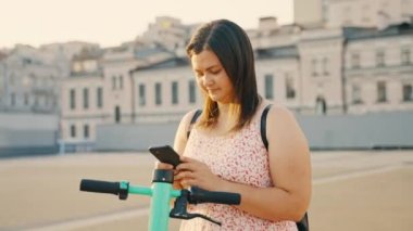 Bir kız elektrikli scooter kiralayıp akıllı telefonundaki bir uygulamayla kilidini açıyor. Modern şehir ulaşımı. Ekolojik nakliye. Yüksek kalite 4k görüntü