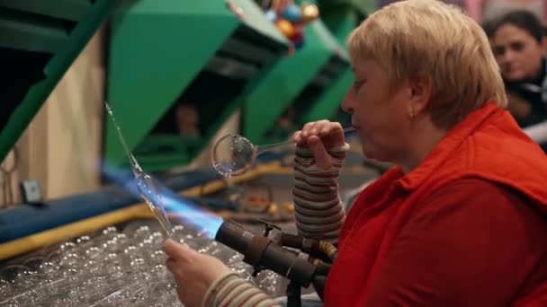 女性労働者は火のバーナーでガラスを加熱することによってクリスマスのガラスのおもちゃを吹く ガラスの新年のおもちゃの製造 グラスブロワー 高品質4K映像 — ストック動画