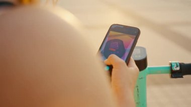 Bir kız elektrikli scooter kiralayıp akıllı telefonundaki bir uygulamayla kilidini açıyor. Modern şehir ulaşımı. Ekolojik nakliye. Yüksek kalite 4k görüntü