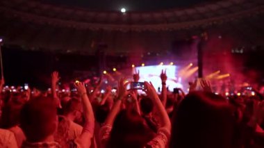 Kalabalık dans ediyor, konserde ellerini kaldırıyor. Parlak renkli sahne ışıklandırması. Eğlence. Aydınlatılmış sahne ışıkları. Konser kalabalığı siluetleri. Yüksek kalite 4k görüntü