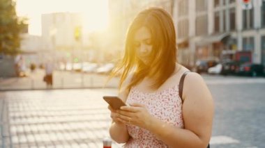 Kız, sosyal ağlar için akıllı telefon kullanıyor. Şehrin caddesinde dikilip gelen mesajdan gülümsüyor. Modern teknolojiler. İnternet iletişimi. Yüksek kalite 4k görüntü