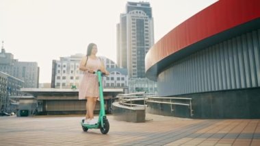 Bir kız elektrikli scooterla modern bir şehrin sokaklarında geziyor. Elektrikli scootera biniyor. Eğlence, eğlence. Yüksek kalite 4k görüntü