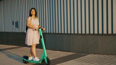 Güneşli bir günde elektrikli scooter süren neşeli bir kızın yavaş çekimleri. Elektrikli scooter süren. Eğlence, eğlence. 4k biçiminde yüksek kaliteli atış
