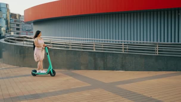 一个女孩在阳光下骑电动车穿过一座现代城市的街道 骑电动车 高质量的4K镜头 — 图库视频影像