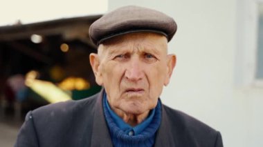 Çok yaşlı ve yalnız bir adamın portresi. Sokakta dikilip kameraya bakan dalgın yaşlı bir adamın yüzünü yakından çek. Yüksek kalite 4k görüntü