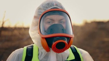 Koruyucu kimyasal giysili bir adam başını çevirip kameraya bakıyor. Dışarıda solunum cihazına bağlı bir adamın portresi. Kameraya bakıyorum. Kirli bölge. Yüksek seviyede radyasyon. Yüksek kalite 4k