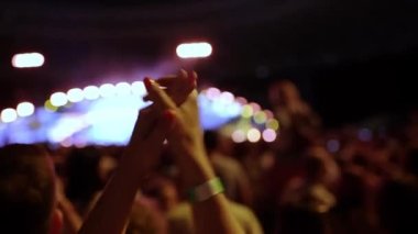 Büyük bir sahnenin önünde dans eden ve alkışlayan bir hayranın ellerinin silueti. Sahne arkası, sahne ışığı, bir konser performansının parlak ışıklandırması. Yüksek kalite 4k görüntü