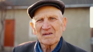 Şapkalı, iç çeken yaşlı bir adamın portresi. Kameraya yakından bakan yaşlı bir adamın buruş buruş yüzü. Yalnızlığın üzüntüsü. Büyükbaba portresi. Yüksek kalite 4k görüntü