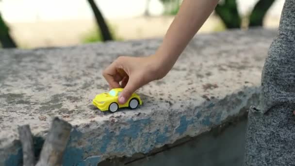 一个小孩的小手把一辆黄色的玩具车沿着室外公园的混凝土栅栏滚动着 快乐童年的概念 高质量的4K镜头 — 图库视频影像