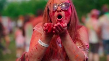 Sarışın ve havalı güneş gözlüklü güzel bir genç kız ellerinde Holi pudrası üflüyor ve gülüyor. Holi renk festivali. Eğlenceliydi. Yüksek kalite 4k görüntü