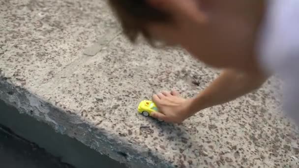一个小孩的小手把一辆黄色的玩具车沿着室外公园的混凝土栅栏滚动着 快乐童年的概念 高质量的4K镜头 — 图库视频影像
