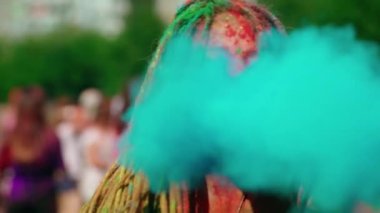 Rasta bukleli güzel bir genç kız, çok renkli tozla kaplanmış, ellerinde renkli Holi tozu üflüyor ve gülüyor. Holi renk festivali. Çok komik. 4k biçiminde yüksek kaliteli atış