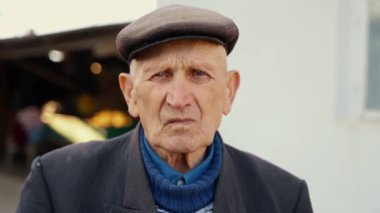 Çok yaşlı ve yalnız bir adamın portresi. Sokakta dikilip kameraya bakan dalgın yaşlı bir adamın yüzünü yakından çek. Yüksek kalite 4k görüntü