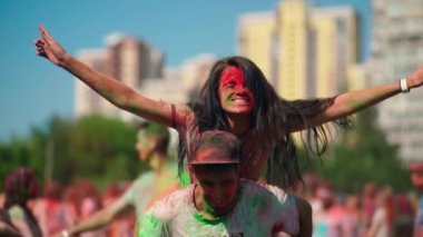 Close front view of young guys covered in holi colors smiling and laughing together. The guy holds the girl in his arms during the celebration of the Holi festival. High quality 4k footage