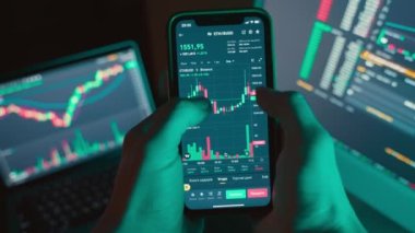 Trader using computer and mobile phone invests in cryptocurrency,stock market and stock exchange in a dark room.Scaling and analyzing the cryptocurrency chart on the phone screen.4k