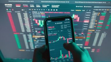 Cryptocurrency charts on mobile phone and computer monitor. Unusual lighting falls on the hands of a man and a telephone. Cryptocurrency tracking. High quality 4k footage