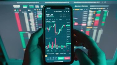 A trader is reviewing on a mobile phone and a computer screen graphs of the growth and fall of the cryptocurrency stock market. Analysis of the cryptocurrency chart on the phone screen. 4k