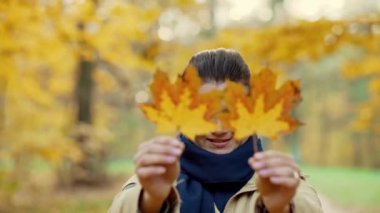 Sarı akçaağaç yaprağı tutan bir kızın portresi. Kız kapanıyor ve gülümsüyor. Autumn Park 'ta. Eğlenceliydi. Yüksek kalite 4k görüntü