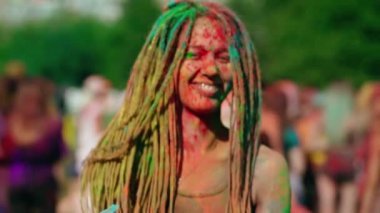A beautiful young girl with dreadlocks, covered in multi-colored powder, throws Holi blue powder at the camera and laughs. Holi festival of colors. Funny. High-quality shooting in 4k format
