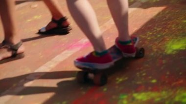 Slow motion of a skateboarder riding on a colorful Holi road at a festival through a crowd of people.Fun and sport concept. High quality 4k footage
