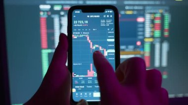 A trader is reviewing on a mobile phone and a computer screen graphs of the growth and fall of the cryptocurrency stock market. Analysis of the cryptocurrency chart on the phone screen. 4k