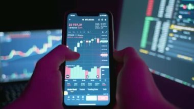 Trader using computer and mobile phone invests in cryptocurrency,stock market and stock exchange in a dark room.Scaling and analyzing the cryptocurrency chart on the phone screen.4k