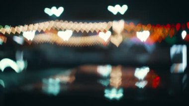 Abstract bokeh effect. A car drives by in defocused road lights in the shape of a heart. Bokeh of road colored lights. Valentines Day. Love or romantic background. High quality 4k footage.