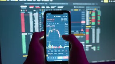 Cryptocurrency stock market on mobile phone screen.bA people sits at home with a laptop and phone, watching cryptocurrency trading.Stock market chart of Bitcoin currency. High quality 4k footage