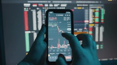 Cryptocurrency stock market on mobile phone screen.bA people sits at home with a laptop and phone, watching cryptocurrency trading.Stock market chart of Bitcoin currency. High quality 4k footage